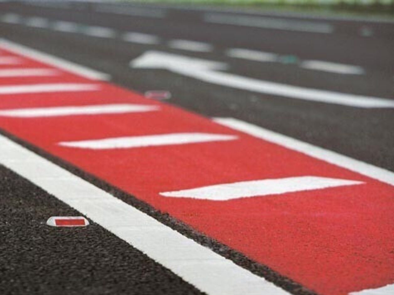 Close-up of Prismo Textureflex red high friction surfacing with directional arrows at a motorway junction, enhancing safety and skid resistance.